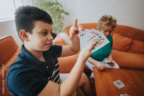 Young boy enjoying a game of cards with his grandmother in a warm, inviting living room setting. Focused interaction and family bonding.