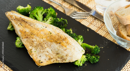 Fried fillet of sea bass with garnish of broccoli on black warm stone plate photo