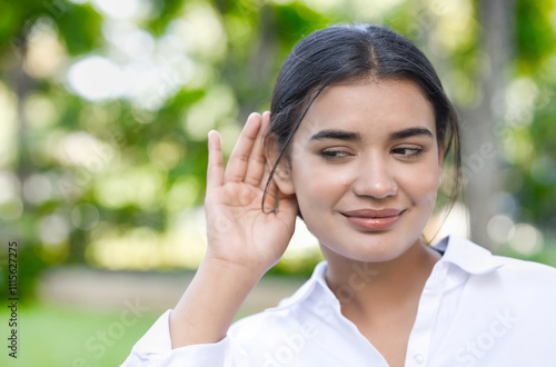 Happy South Asian Indian woman hearing or listening with happy smiling positive mood, feeling good in summer outdoor green city surroundings photo