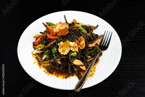 Stir fry black noodles seafood and vegetables in white bowl on dark background