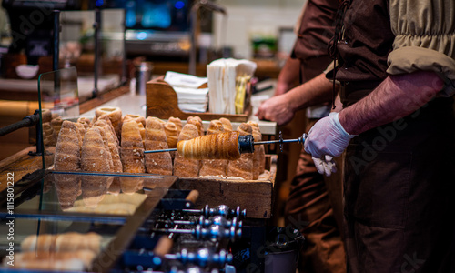 Street food of Prague. Traditional national Czech sweet food. Tubes of sweet dough, cooked on an open fire. Popular dessert in Prague. Grilled food. Manufacturer trdelnik. Selective focus.