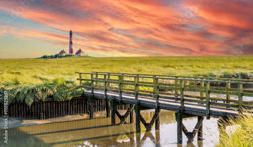 View of the Westerheversand lighthouse on the North Sea with salt marshes and a small wooden bridge photo