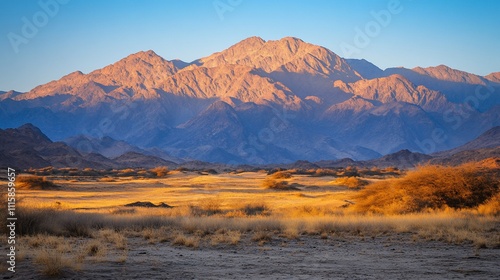 Dramatic mountain range at sunrise over a golden, dry desert landscape.