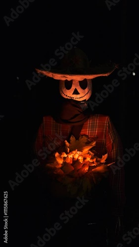 A Halloween character with a pumpkin body and a white skull-like face wearing a hat, red shirt, and sweater holds glowing autumn yellow leaves in hands, creating an eerie and festive atmosphere.