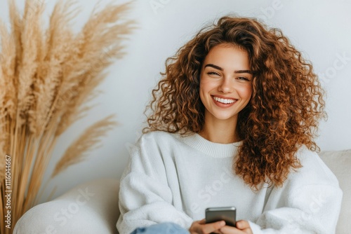 Smiling woman engaging with her smartphone while relaxing on a couch in a coz...