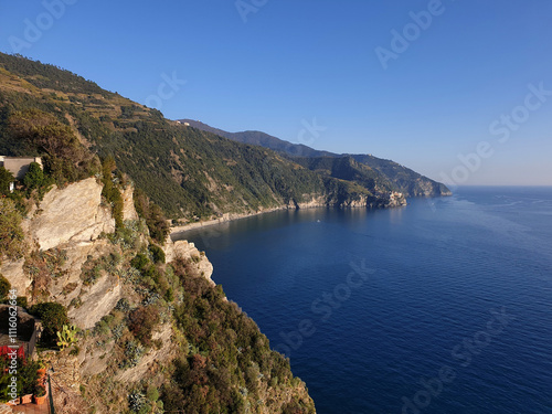 Billede på lærred A breathtaking coastal view showcasing the rugged cliffs and verdant hills of the Cinque Terre region, overlooking the tranquil Ligurian Sea under a clear blue sky