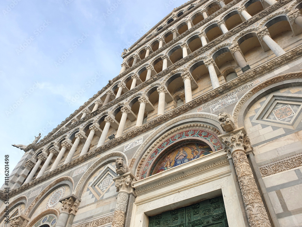 Fototapeta premium A detailed close-up of the ornate facade of the Pisa Cathedral, showcasing exquisite Romanesque architecture, decorative arches, and intricate stone carvings under a clear blue sky.