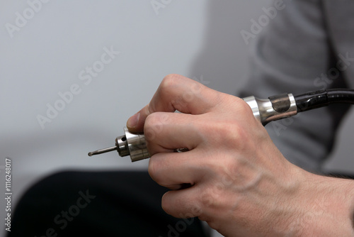 A drill press with a drill bit in the hands of a man close-up.
