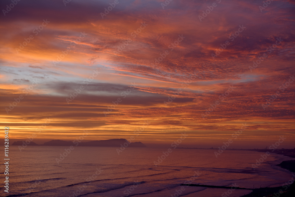 Obraz premium As the sun sets over San Lorenzo Island, the view from Miraflores becomes pure magic .The island silhouettes against a sky ablaze with color, while the ocean whispers of infinite horizons. 