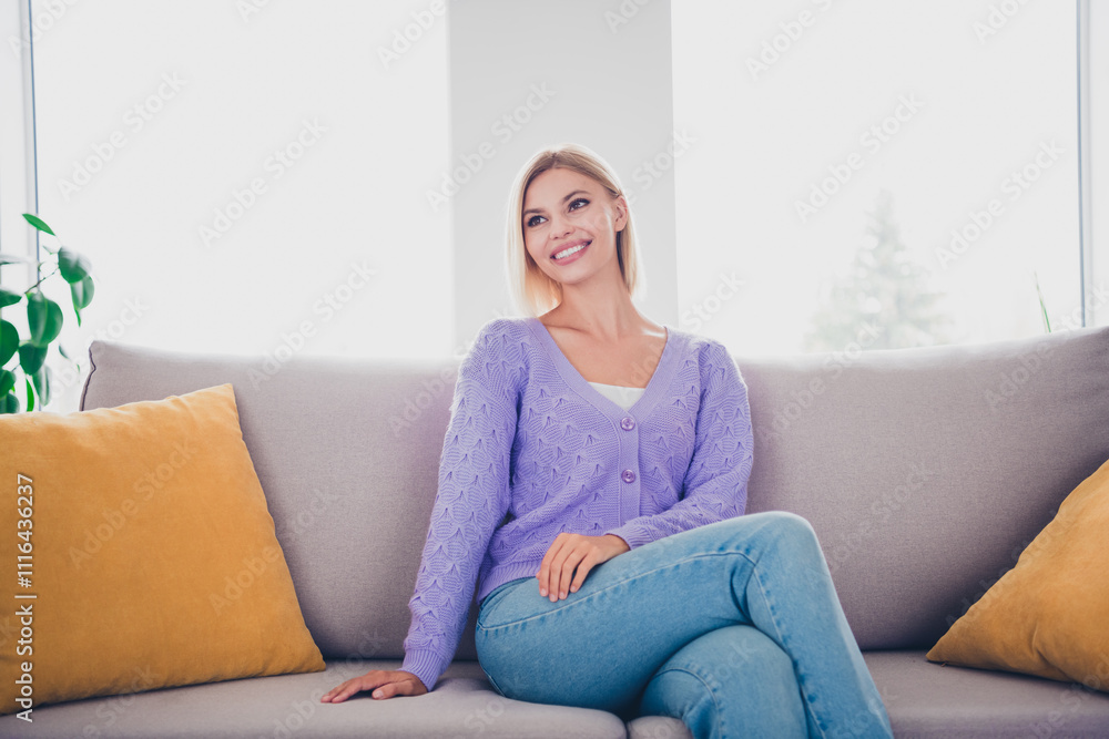 Attractive young woman with blond hair smiling in a living room setting, wearing a knitted sweater, enjoying a relaxed day indoors Attractive young woman with blond hair smiling in a living room setting, wearing a knitted sweater, enjoying a relaxed day indoors