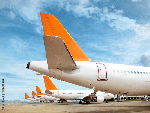 Multiple commercial airplanes lined up on the airport apron. Tail view with bright orange rudders under blue sky. Aviation and transportation concept.