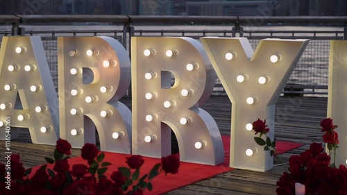 The romantic proposal includes Marry Me letters with rose petals and candles against a city skyline. The scenery creates a perfect setting for a special moment of commitment and love
