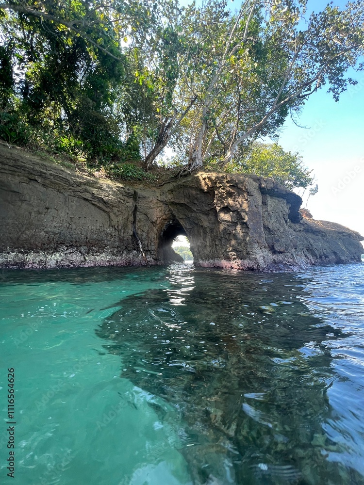 Fototapeta premium Serene view of a natural rock arch framed by lush greenery, showcasing tranquil turquoise waters. Ideal for travel and nature themes, evoking a sense of adventure.