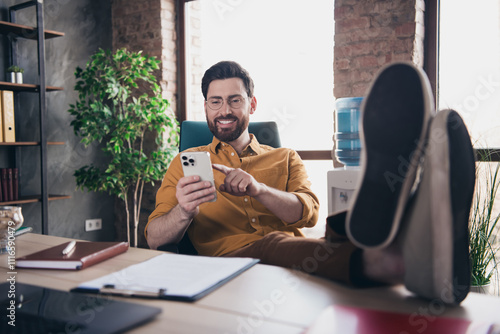 Full length photo of handsome guy hold device relax legs table wear yellow shirt formalwear comfortable startup office loft room interior photo