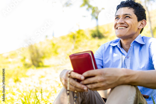 A 30-year-old Latino man holds a Bible in his hands, smiling as he looks at the horizon with happiness and satisfaction, reflecting his union with God during Holy Week in Latin America