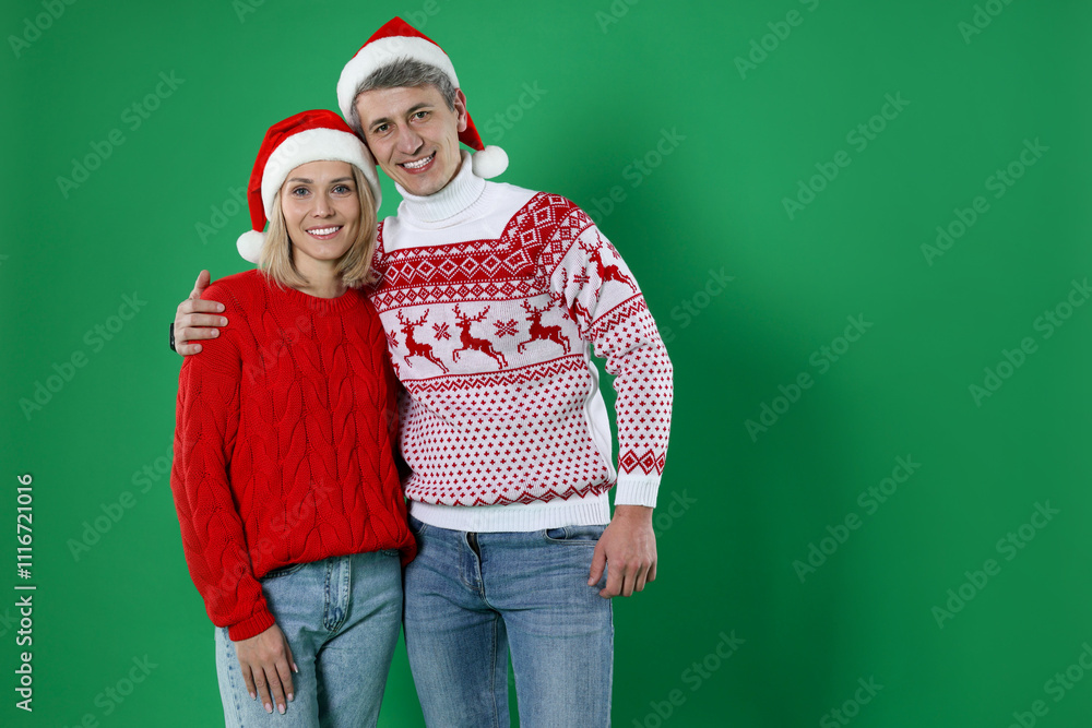 Happy couple in Christmas sweaters and Santa hats on green background. Space for text Happy couple in Christmas sweaters and Santa hats on green background. Space for text