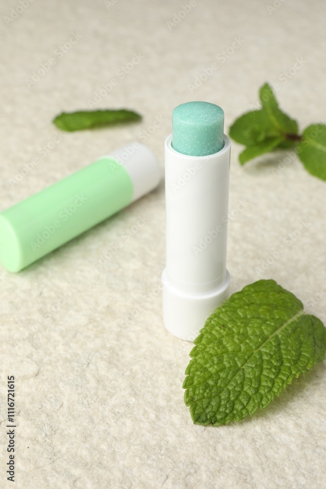 Mint lip balms and green leaves on beige textured table, closeup. Cosmetic product Mint lip balms and green leaves on beige textured table, closeup. Cosmetic product