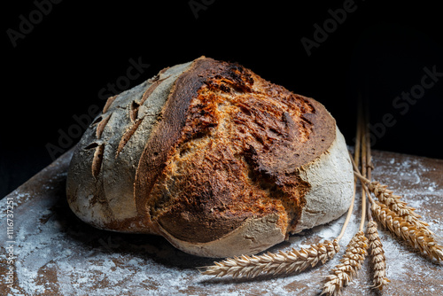 Round loaf of freshly baked sourdough bread with ears of wheat on wooden cutting board, closeup. Rustic sourdough bread. Cooking healthy sourdough bread at home photo