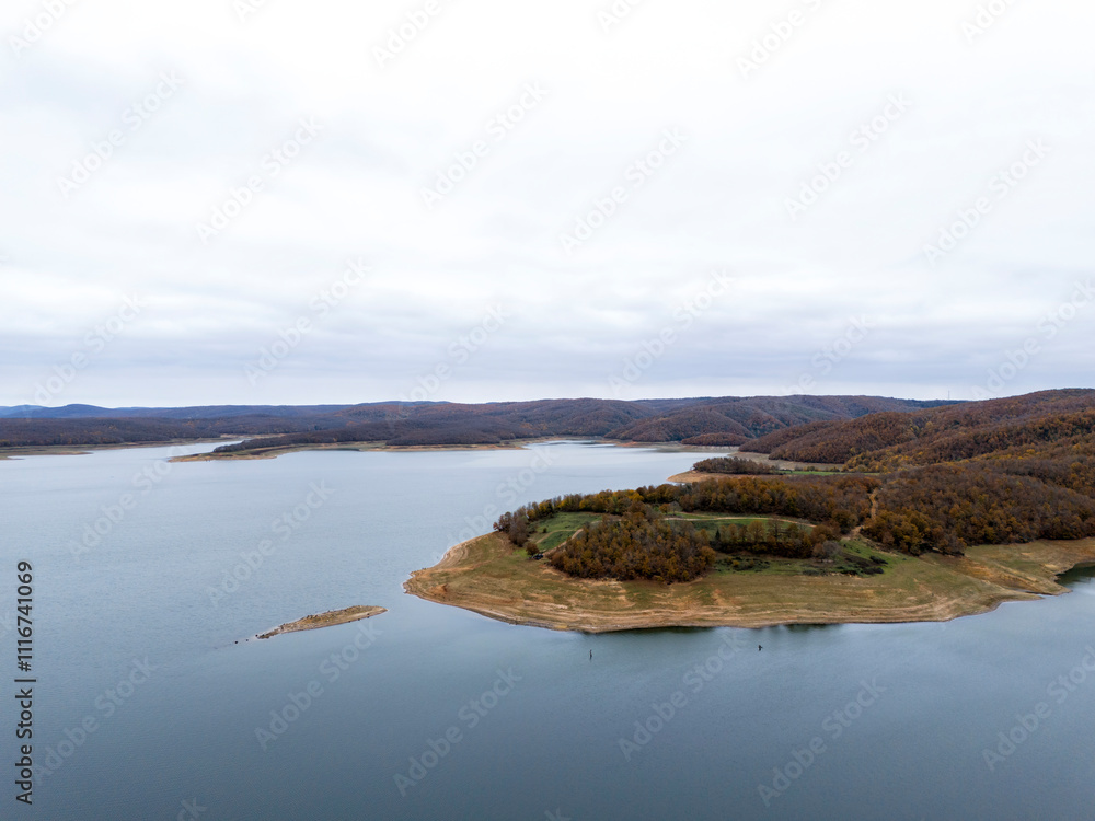 Aerial View of a Tranquil Lakeside Landscape. High-angle, full shot of a serene lake surrounded by rolling hills covered in deciduous trees. Aerial View of a Tranquil Lakeside Landscape. High-angle, full shot of a serene lake surrounded by rolling hills covered in deciduous trees.