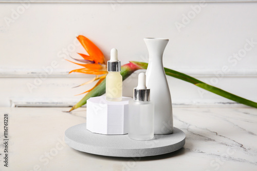 Bottles of cosmetic products with beautiful strelitzia flower, plaster podiums and vase on light background photo