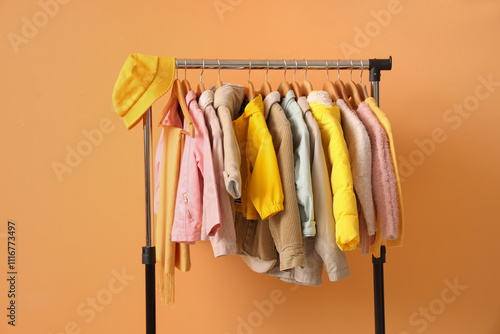 Rack with stylish children's clothes and accessories on orange background