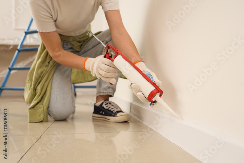 Принти на полотні Young woman applying sealant to baseboard in room