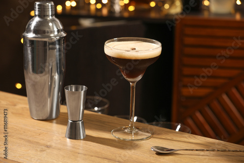 Glass with delicious espresso martini, jigger and shaker on wooden table in bar photo