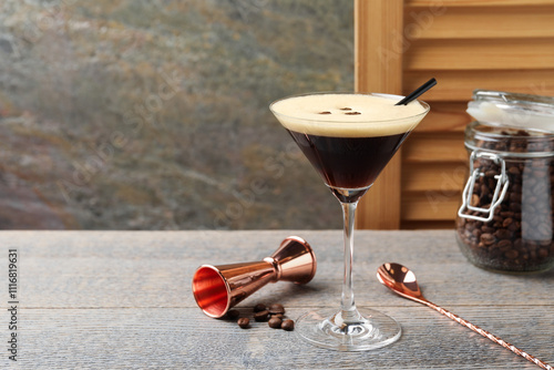 Delicious espresso martini with coffee beans in glass and bartender equipment on wooden table, space for text photo