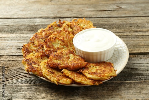 Delicious potato pancakes and sour cream on wooden table, closeup photo