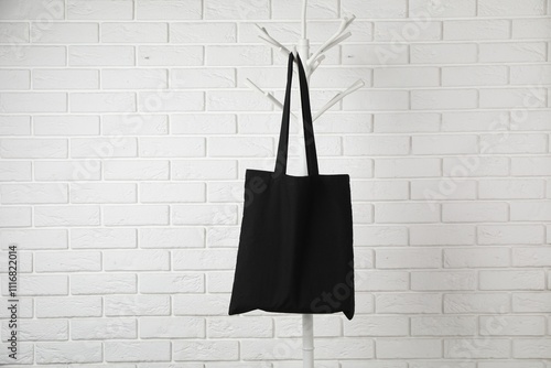 Black eco bag hanging on clothing rack near white brick wall. Mockup for design photo