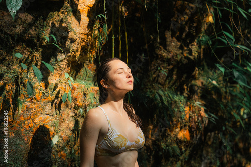 Woman standing under the stream of tropical waterfall enjoying nature photo