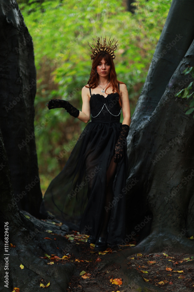Fototapeta premium Young witch with crown on her head in the forest