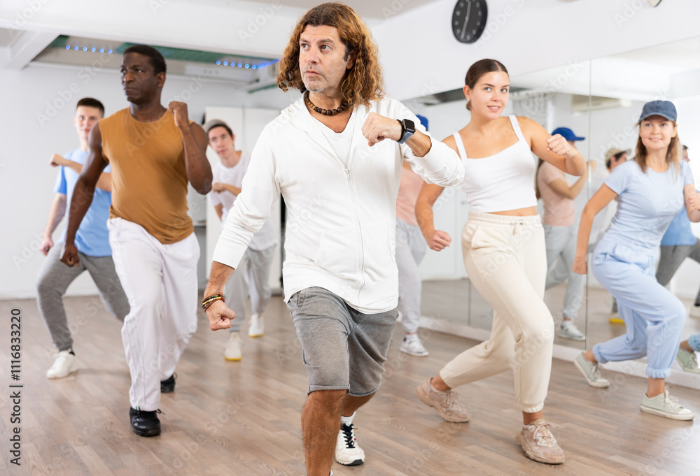 Fototapeta premium Group of sportive young adult diverse dancers performing dynamic movements during aerobic dance workout in gym