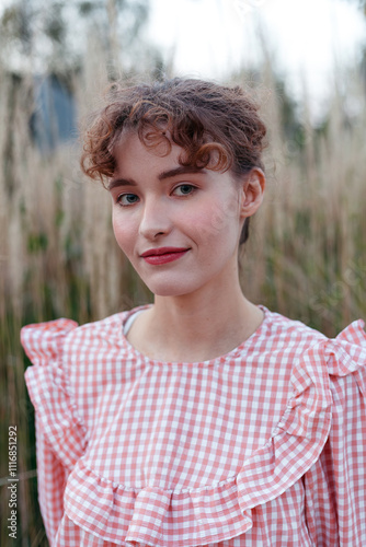 woman wearing a pink gingham blouse stands in tall grass photo