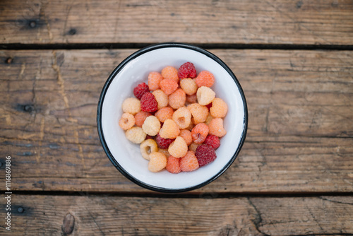 Bowl of assorted fresh raspberries on wooden table. photo