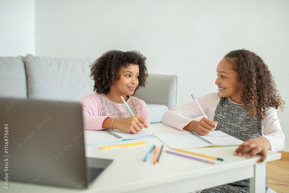 Two young African American girls share a moment of joy and support while working on their homework at a cozy home setting, surrounded by colorful stationery. Two young African American girls share a moment of joy and support while working on their homework at a cozy home setting, surrounded by colorful stationery.