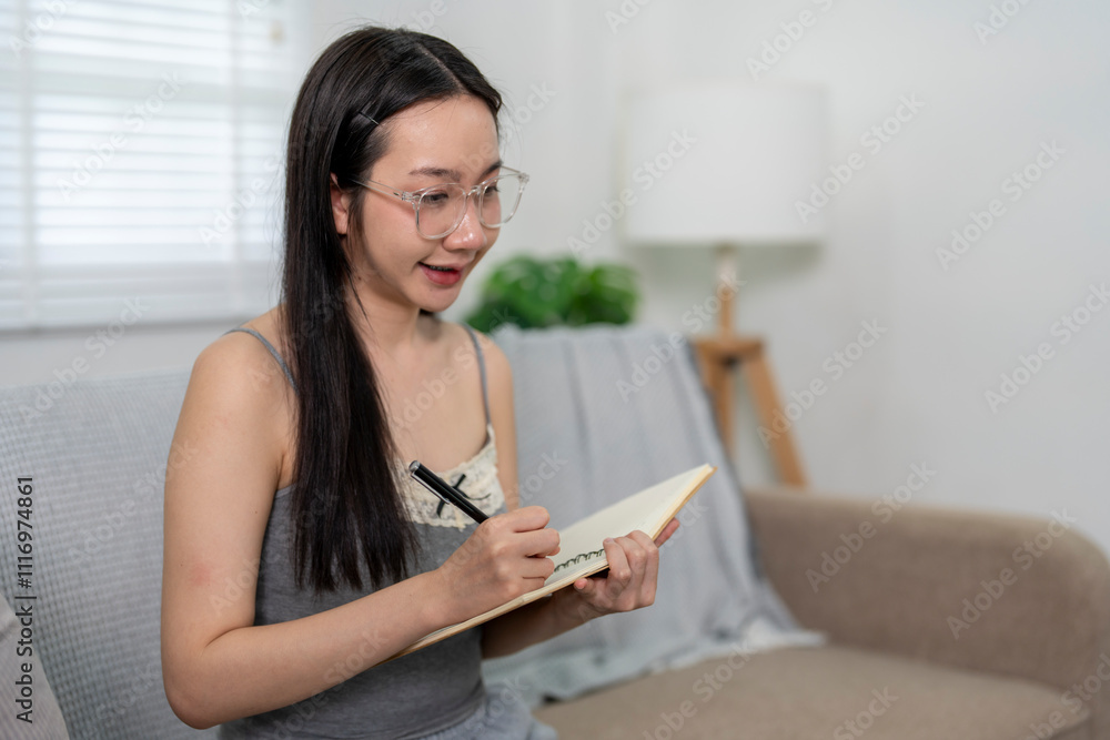 Young woman sitting on sofa taking notes in notebook Young woman sitting on sofa taking notes in notebook