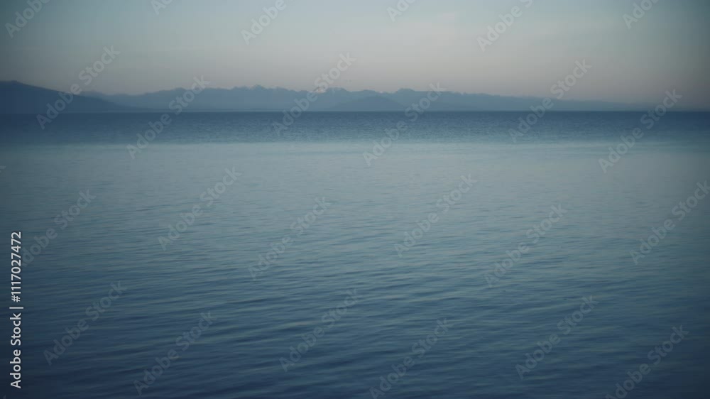 Calm water surface of Pacific Ocean with snowy mountains in the background Calm water surface of Pacific Ocean with snowy mountains in the background