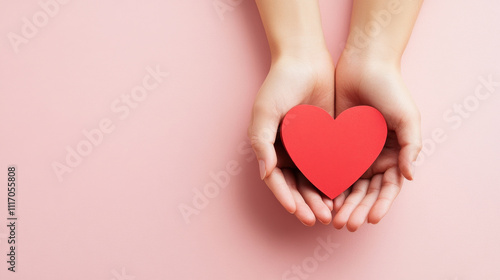 Gently holding red paper heart in two hands, symbolizing love and care. soft pink background enhances emotional expression of affection and warmth photo