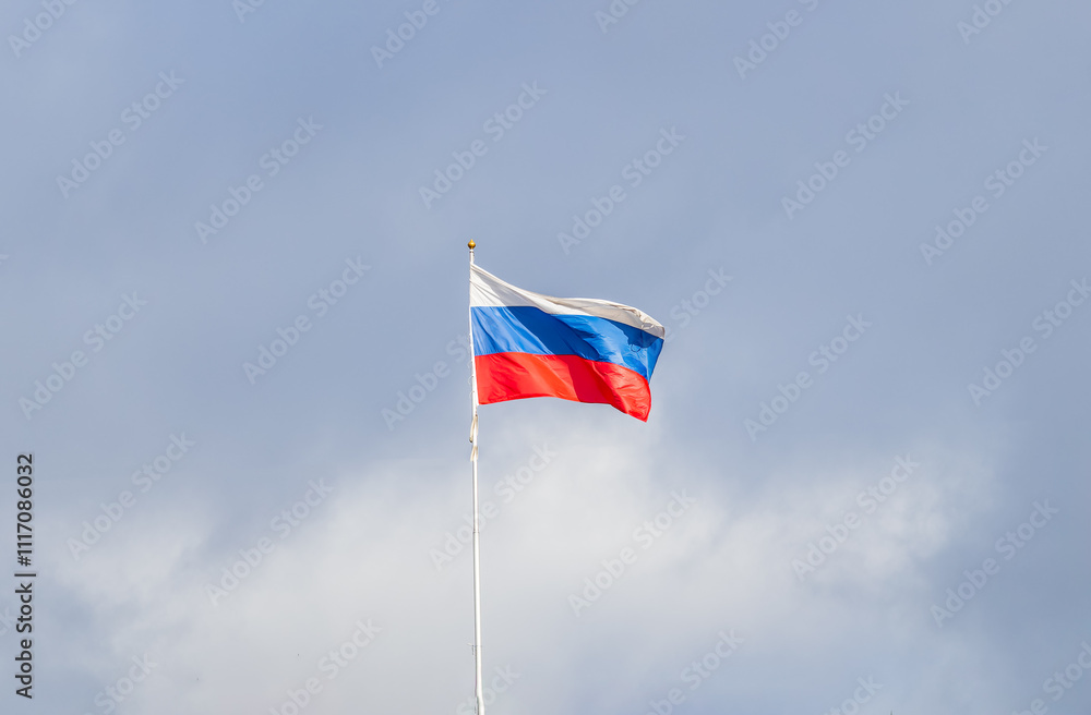 Fototapeta premium Russian tricolor flag waving in the wind against a blue sky.