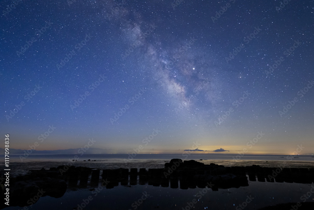 夜明けの能登半島の海辺に光る星あかりと天の川