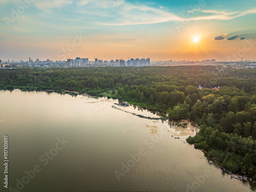 Big lake with green shores in bright sun light and city on horizon, aerial landscape. Recreation concept. Aerial view photo