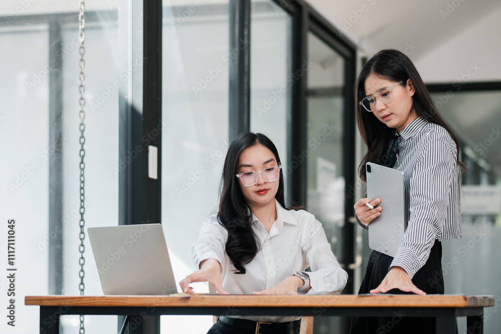 Two businesswomen working together in a modern office, using a laptop and tablet for strategic planning. Two businesswomen working together in a modern office, using a laptop and tablet for strategic planning.