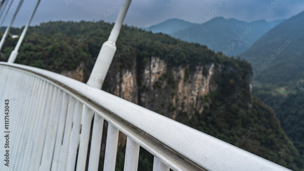Fototapeta premium Details of the architecture of the suspension bridge. White lattice railings and stretched cables against the background of steep cliffs and gorges. Close-up. China. Zhangjiajie Glass Bridge. 