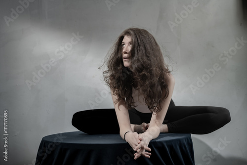 Canvastavla A woman with flowing hair crouches on a round table, engaging in a focused yoga pose dressed in monochrome attire, representing strength and inner reflection
