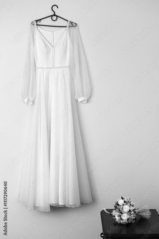 hanging on a black hanger on the wall. The dress has long sheer sleeves and features lace detailing on the bodice and waistband. It looks light and airy. hanging on a black hanger on the wall. The dress has long sheer sleeves and features lace detailing on the bodice and waistband. It looks light and airy.