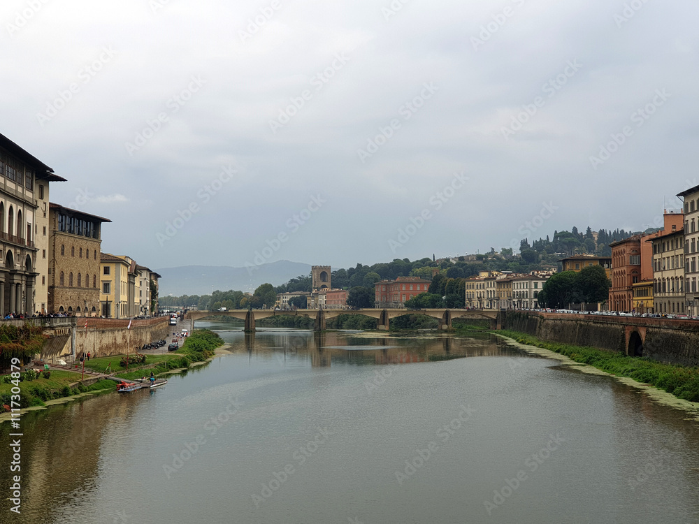Scenic view of the Arno River surrounded by historic buildings and a bridge under a cloudy sky, showcasing the tranquil beauty of Florence's architecture and landscape. Scenic view of the Arno River surrounded by historic buildings and a bridge under a cloudy sky, showcasing the tranquil beauty of Florence's architecture and landscape.