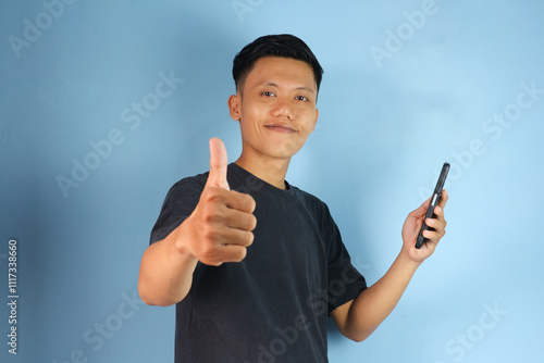 Young Asian man holding his mobile phone with happy expression and thumb up gesture 