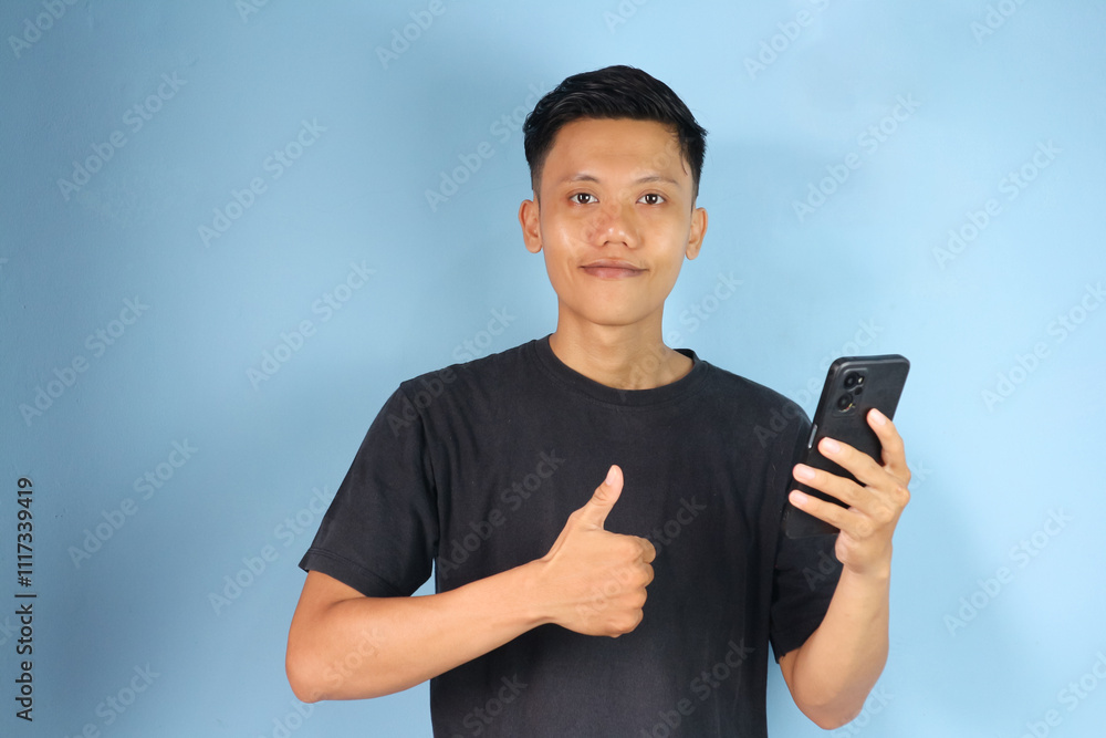 Young Asian man holding his mobile phone with happy expression and thumb up gesture Young Asian man holding his mobile phone with happy expression and thumb up gesture