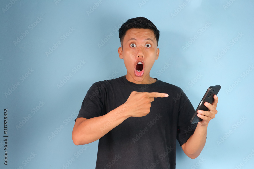 Young Asian man pointing at mobile phone screen with shocked expression Young Asian man pointing at mobile phone screen with shocked expression